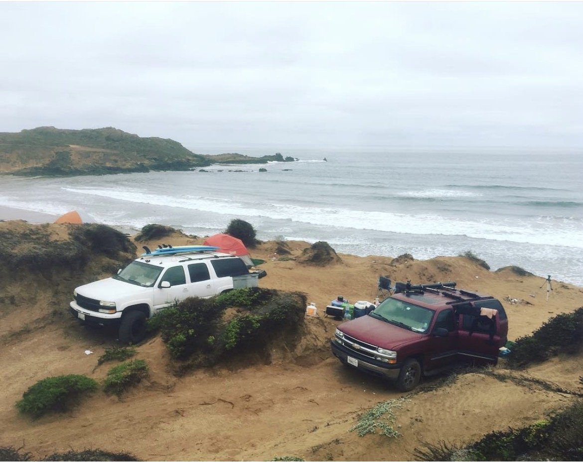Trucks and tents camped above a remote Baja coastline on an Eat Sleep Surf expedition