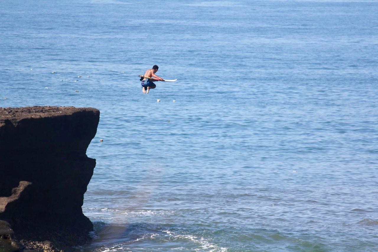 Wayan Dedi jumping off a cliff with a surfboard
