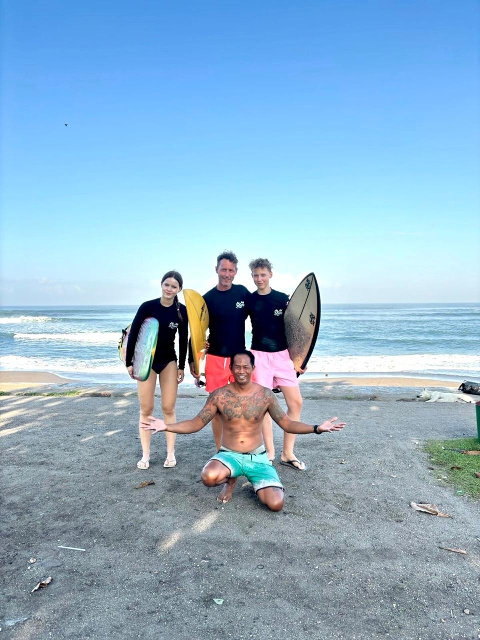 Wayan Dedi kneeling with surf students and boards