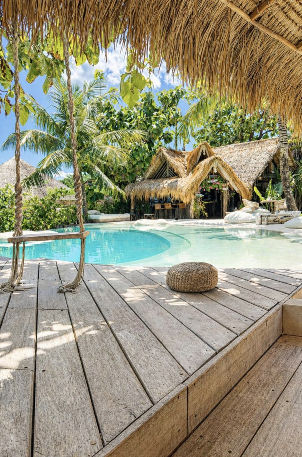 View of the pool and bar from under a thatched roof with a rope swing