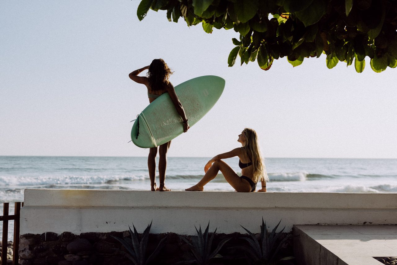 Surfer with a board looking out at the ocean from Coco Surf's beachfront social area