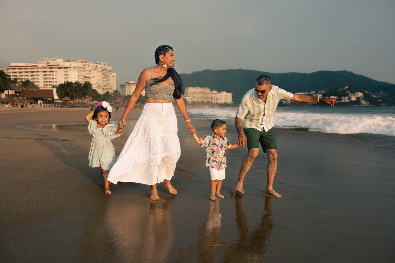 Family of four walking hand-in-hand along the beach at golden hour