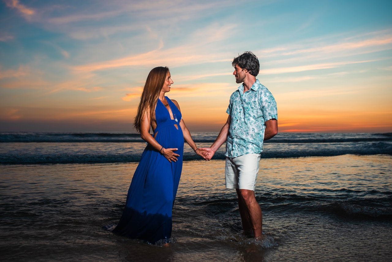 Couple holding hands in the shallows at sunset, maternity portrait