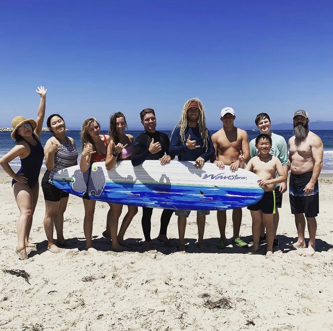 Group of surf students posing with a rental surfboard on an LA beach