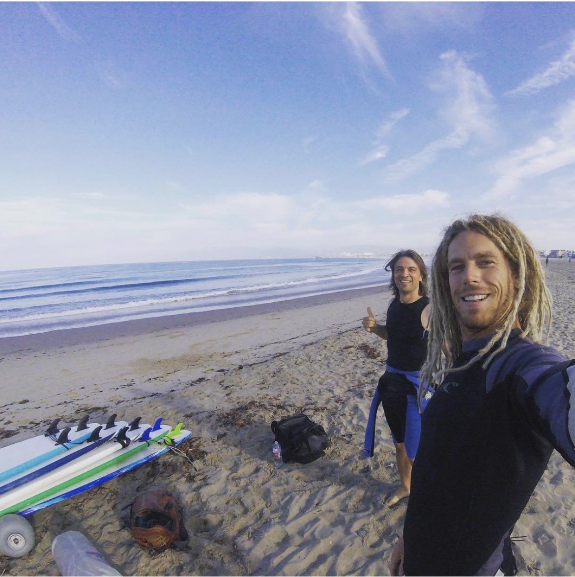 Two Eat Sleep Surf instructors with a stack of surfboards on the beach
