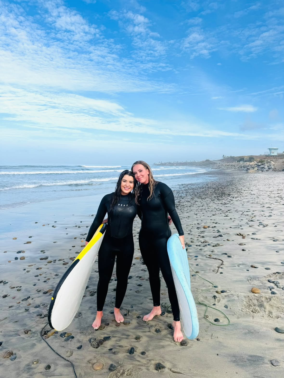 Two Enjoy The Ride students in wetsuits holding their boards on the beach after a lesson
