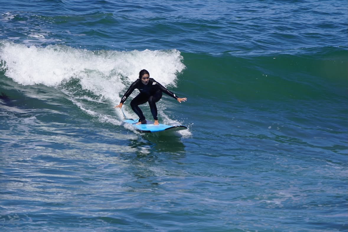 Student riding a small wave on a blue soft-top during an Enjoy The Ride lesson