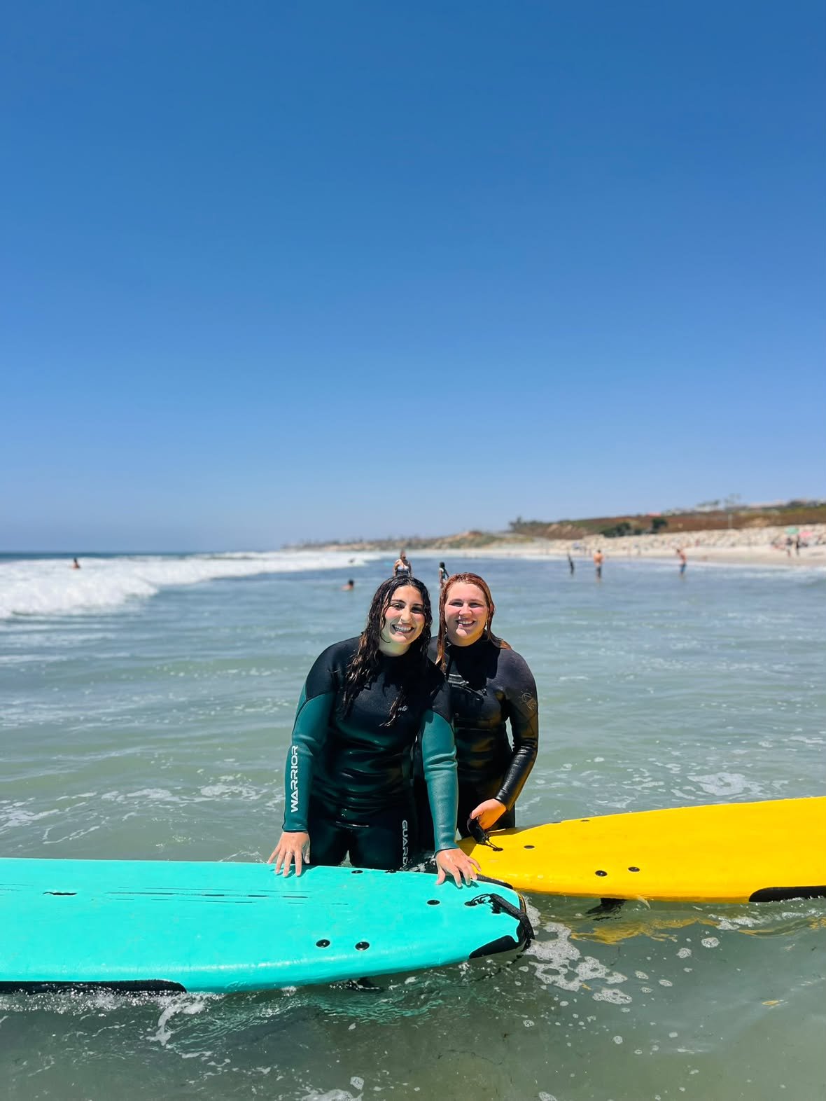 Two smiling students standing in the shallows with a teal and a yellow soft-top