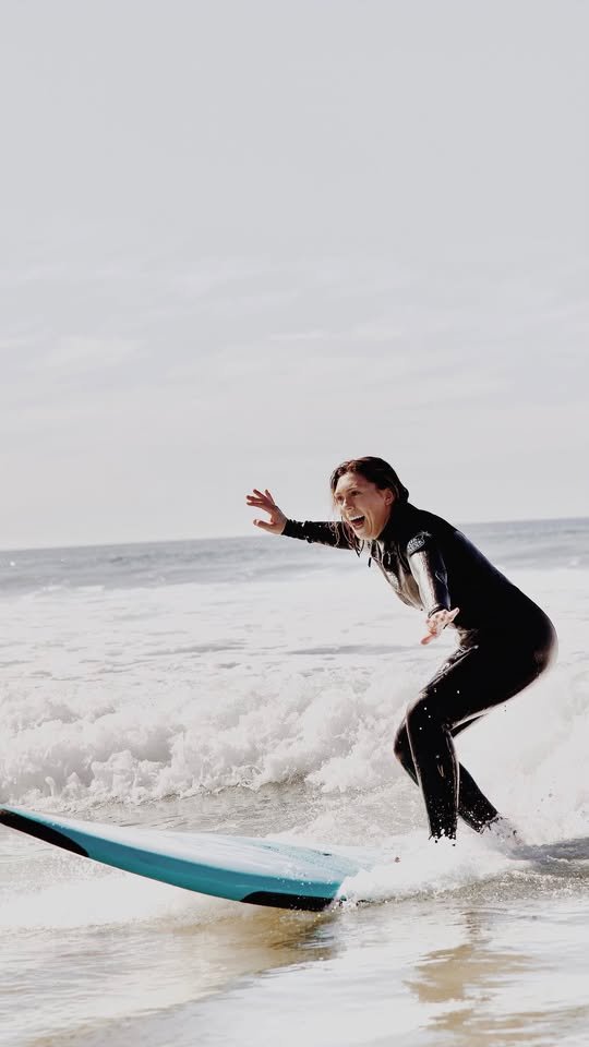 Student laughing while riding a whitewater wave on a teal soft-top