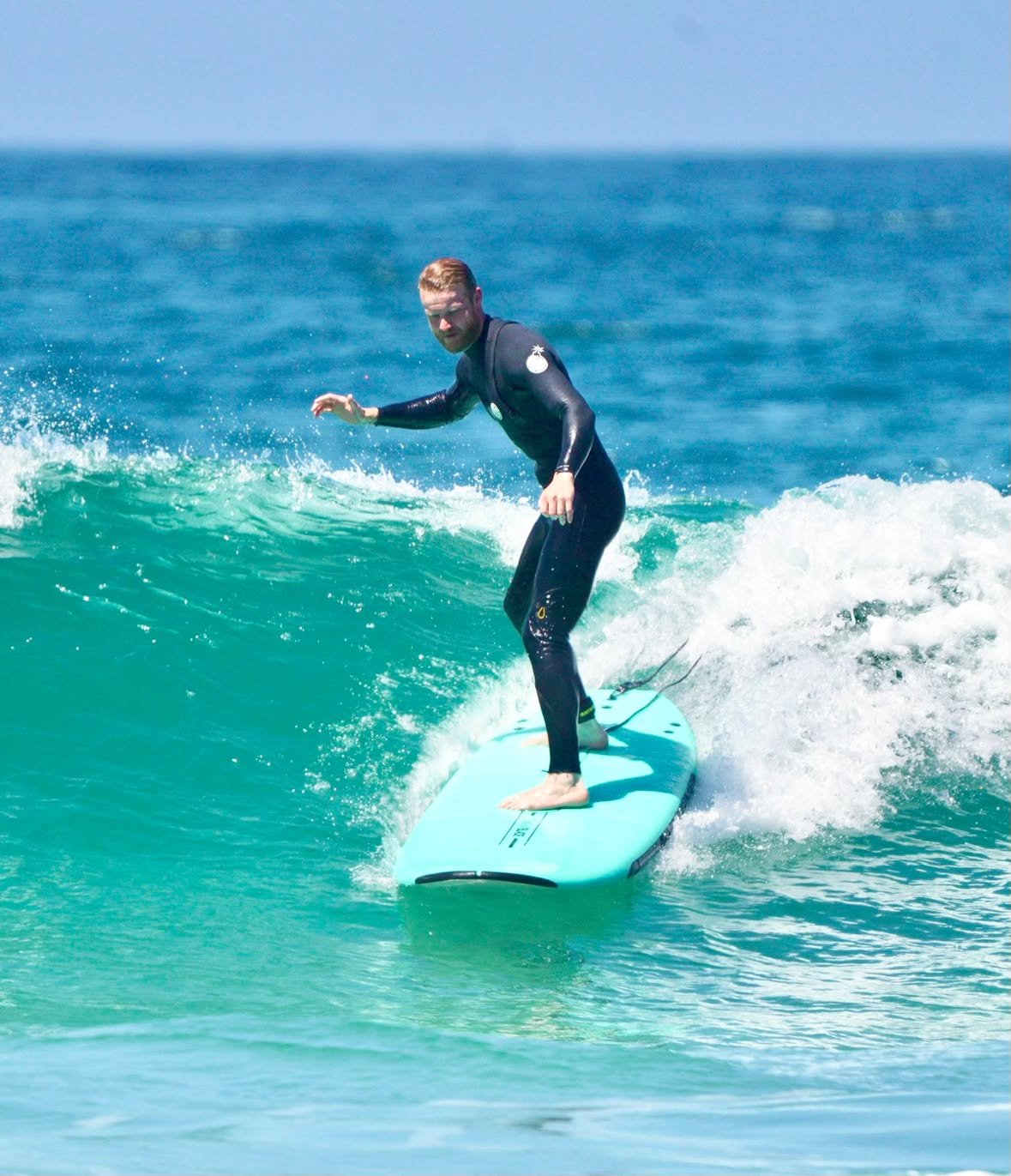 Student riding a green wave on a turquoise soft-top during a coaching session