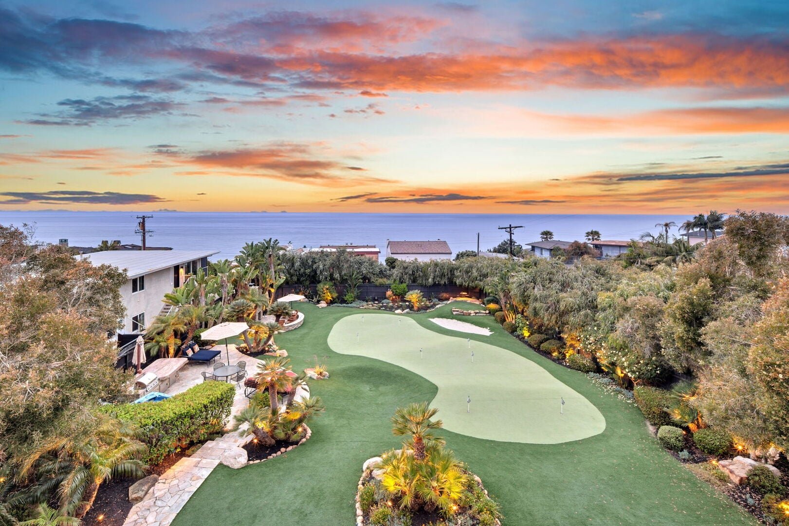 Aerial view at sunset of an Encinitas Haustay home's ocean-view backyard with a putting green