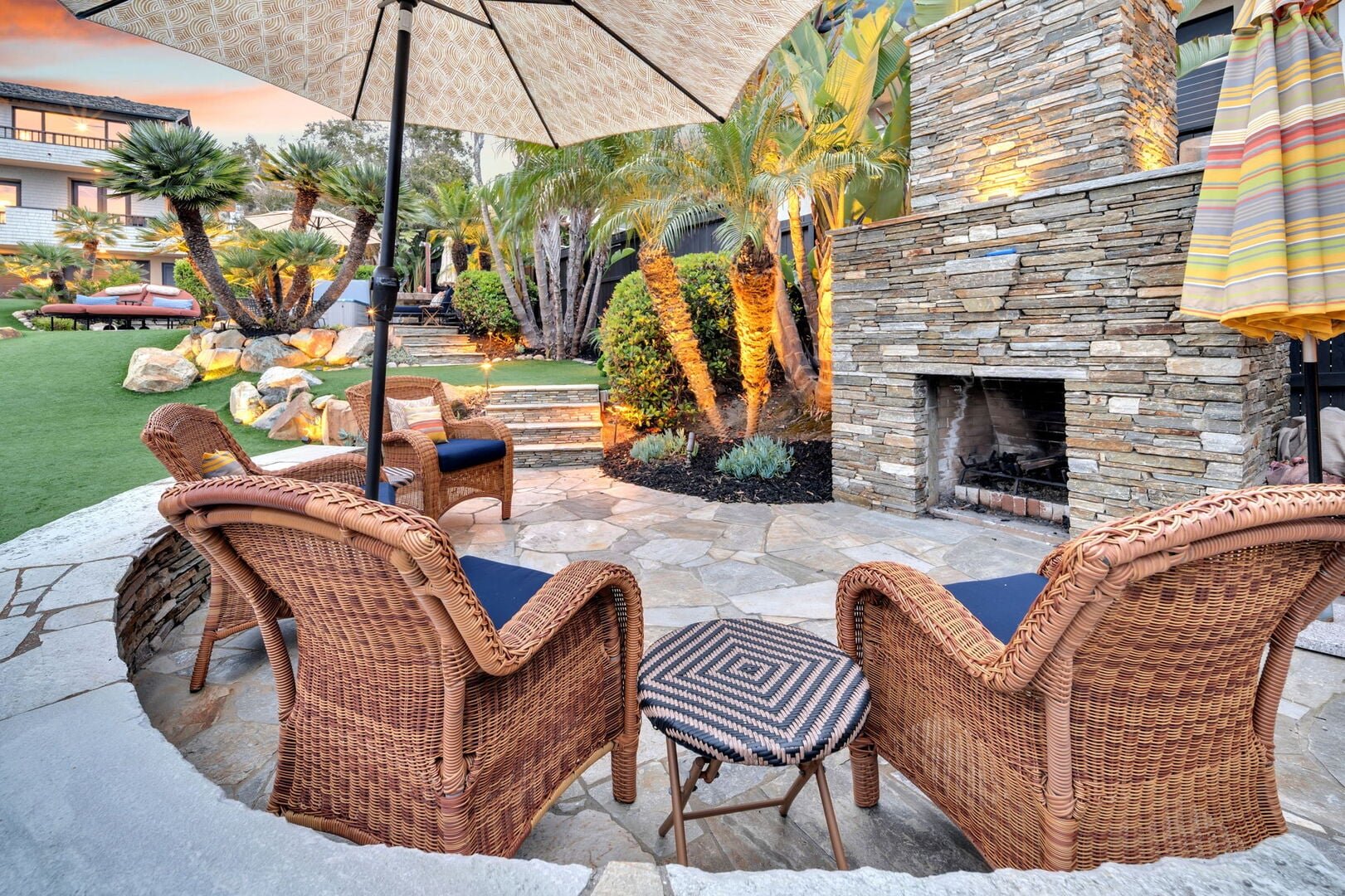 Stone fireplace patio with wicker chairs and an umbrella at an Encinitas Haustay home