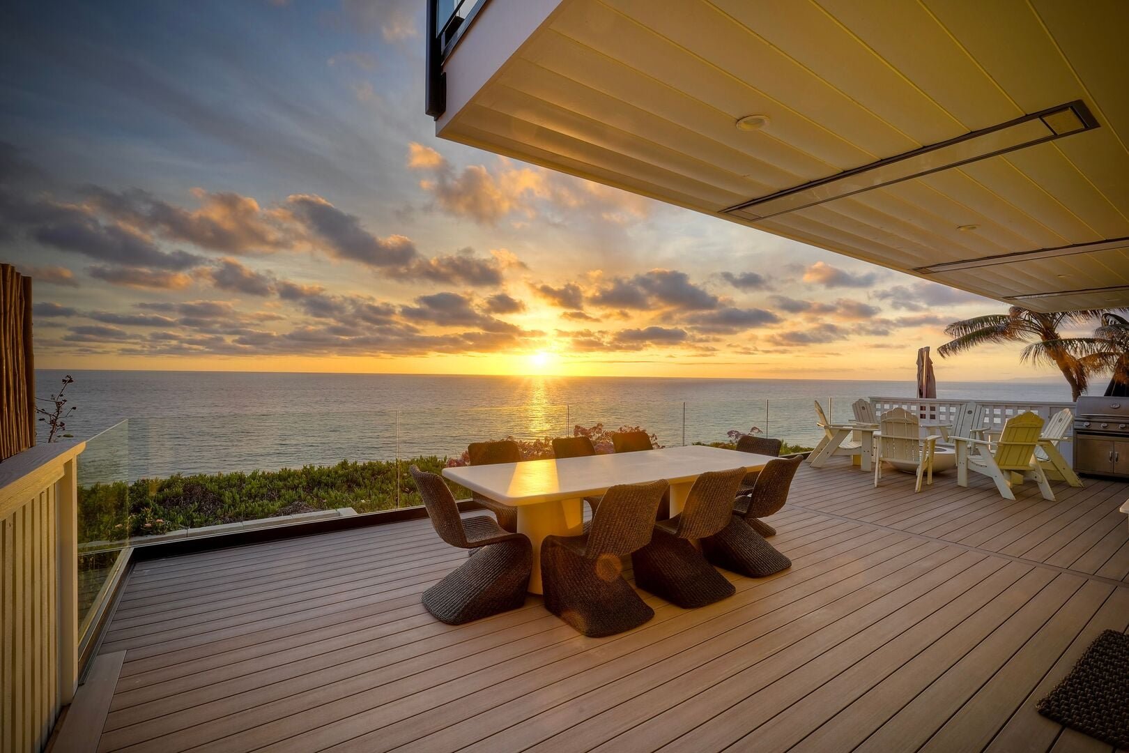 Oceanfront deck with a dining table and fire pit seating at sunset at an Encinitas Haustay home