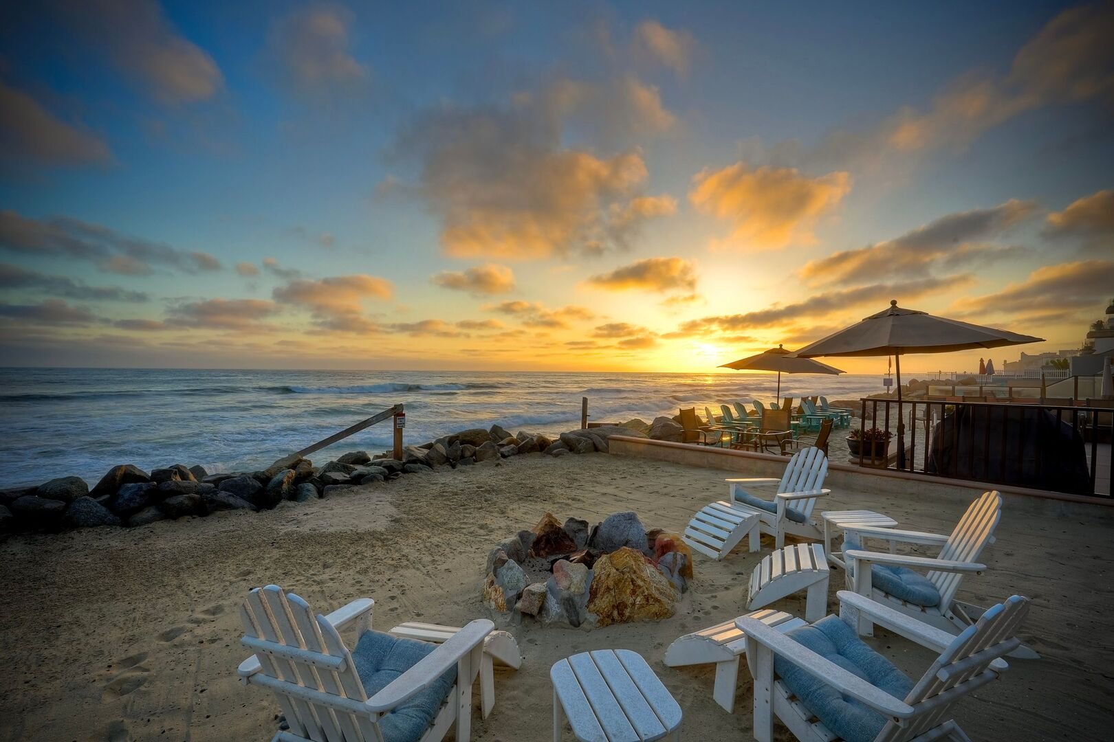 Beachfront fire pit with Adirondack chairs at sunset at an Oceanside Haustay home